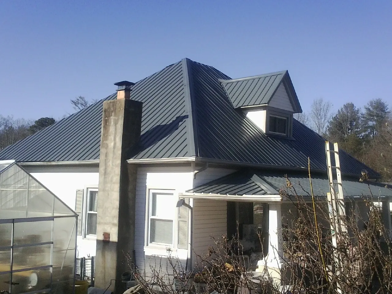 Dark blue standing seam metal roof on a white farmhouse with dormer — Slate & Tile Roof Repair by Roofing Brothers in Plainville