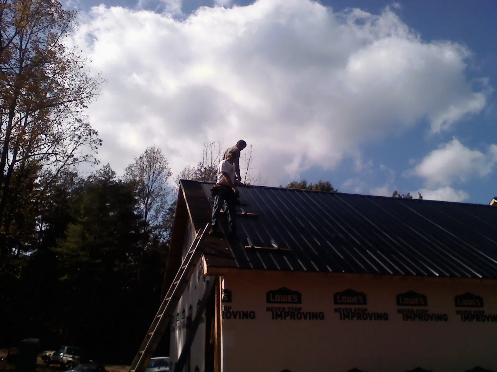 Roofer fastening dark metal panels high against a cloudy sky, from a Roof Inspection job in Plainville