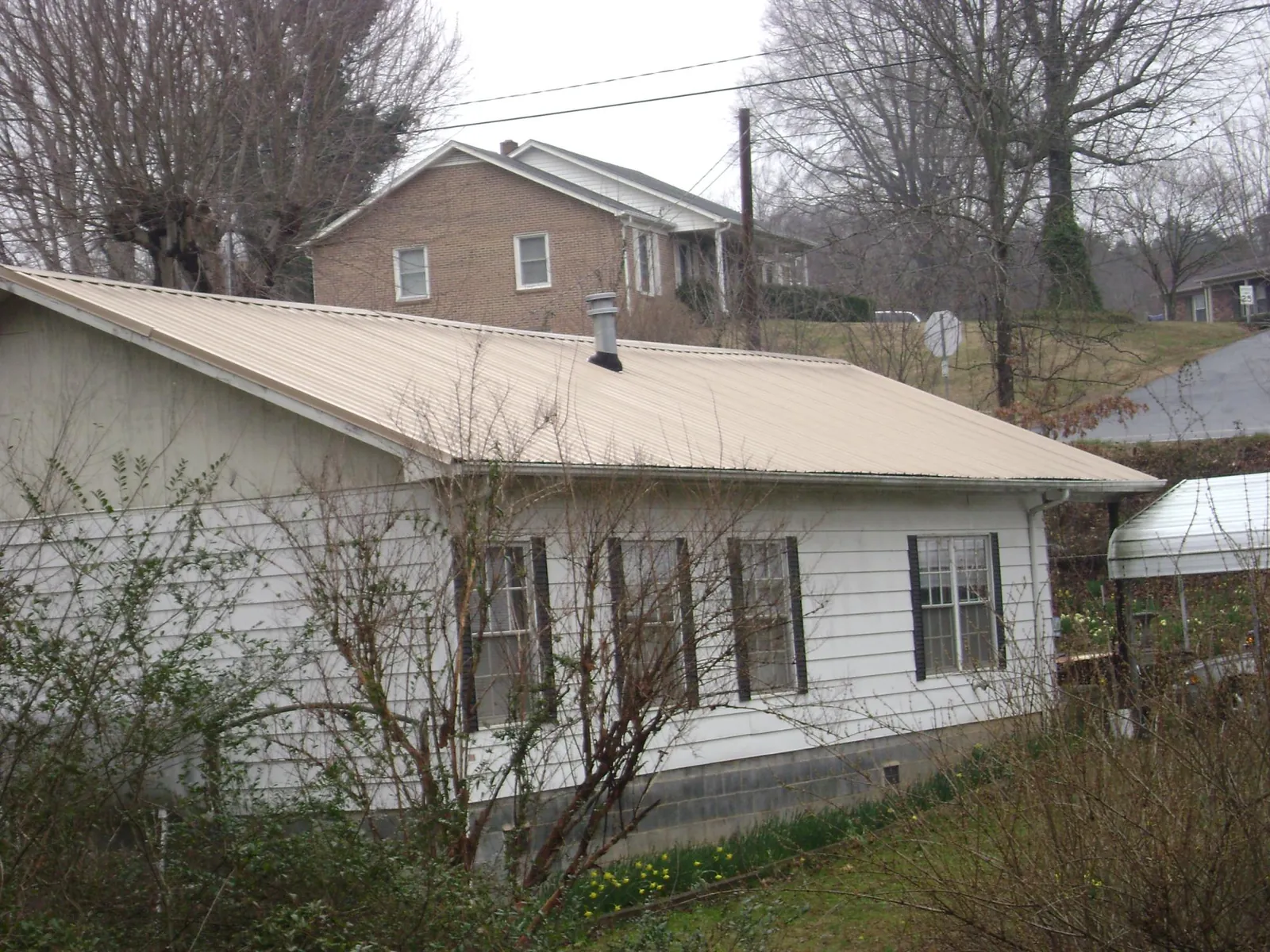 Tan metal roof on a white sided house set into a hillside — Commercial Roofing by Roofing Brothers in Plainville